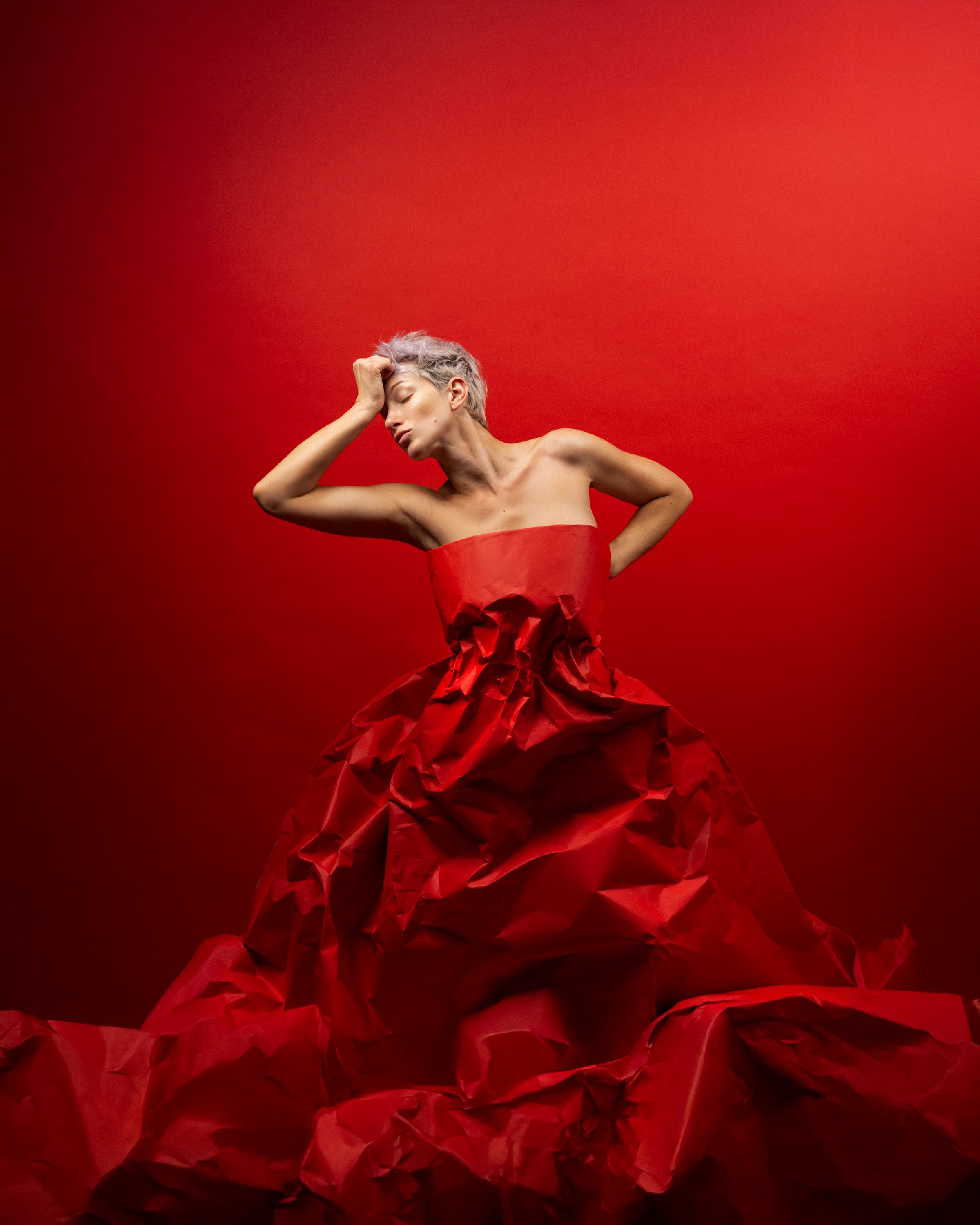 A figure surrounded by flowing red fabric against a red backdrop