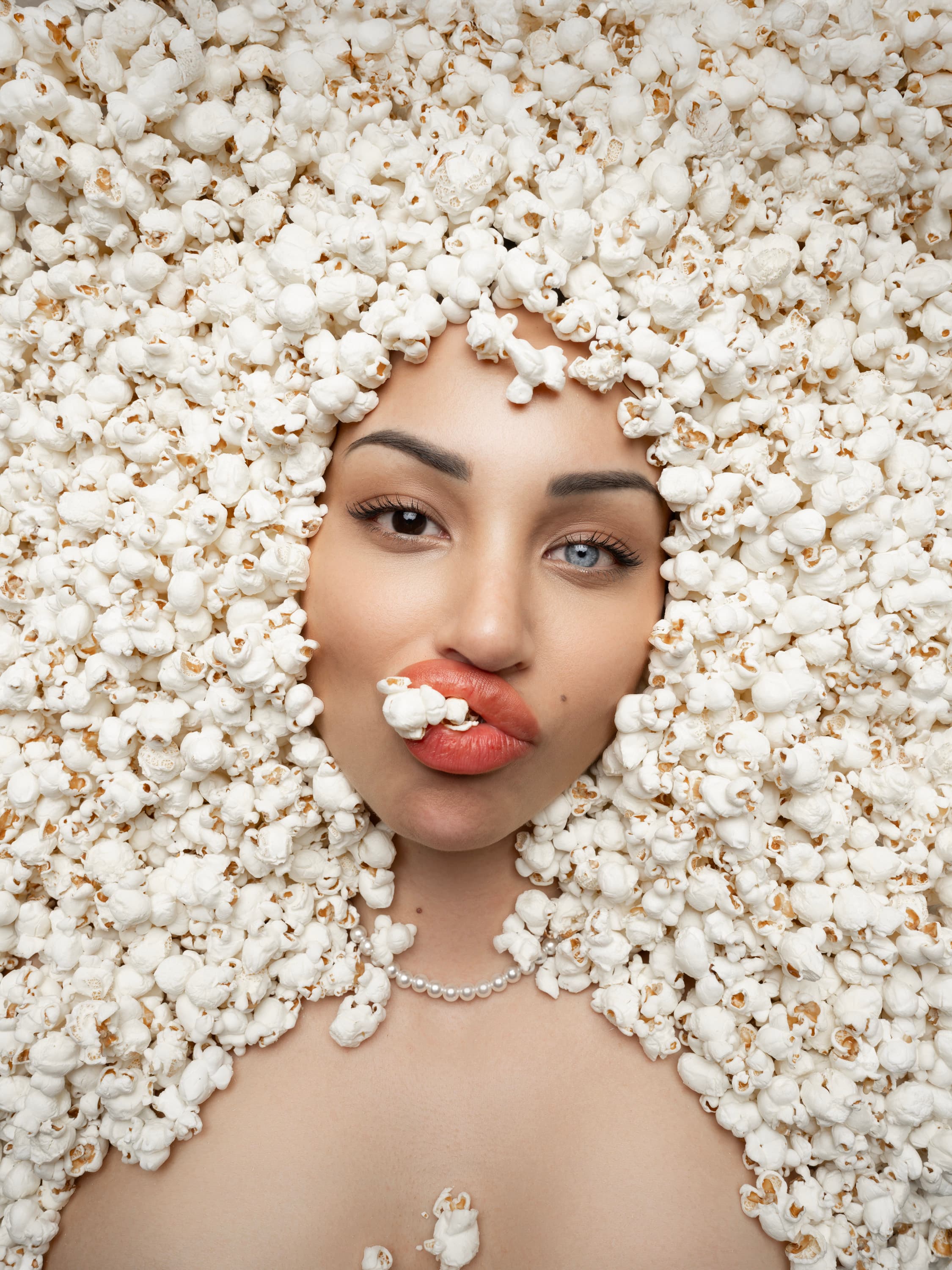 A woman's face framed by a halo of popcorn, with a piece held between her lips