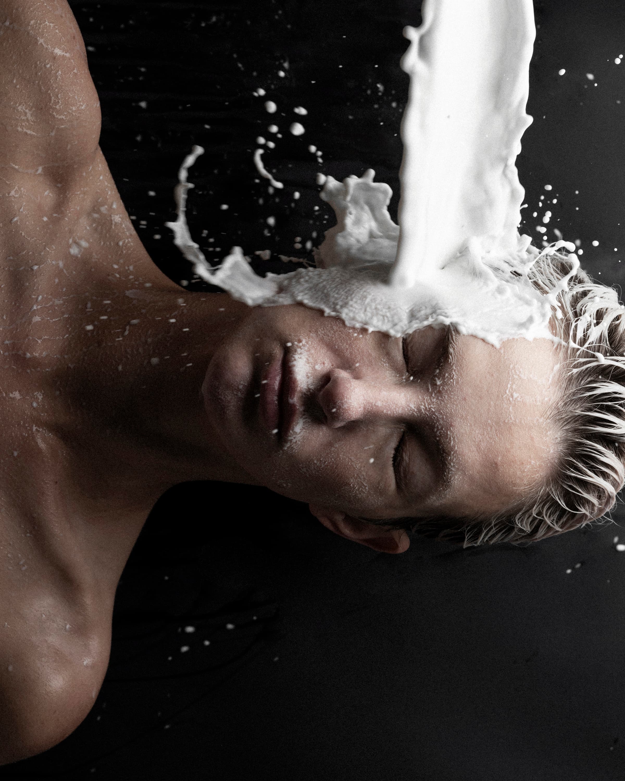 A face turned sideways as milk pours onto the cheek and splashes across the skin