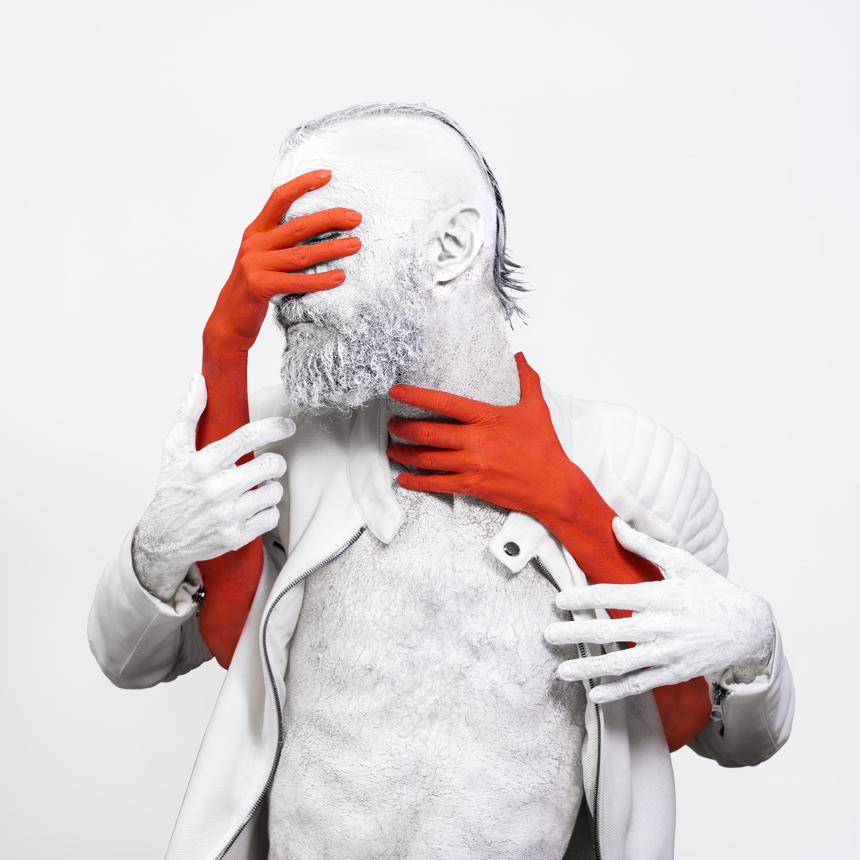 A figure painted white in a white jacket, hidden behind rust-red hands